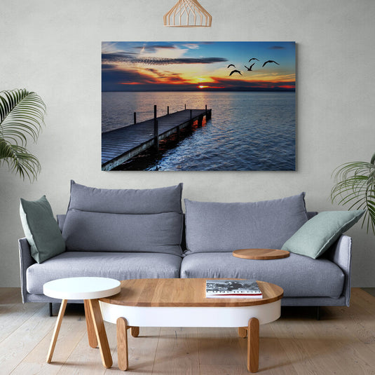Fotografía de atardecer con muelle y aves en vuelo sobre mar en calma