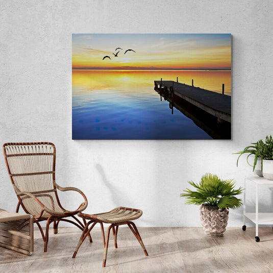 Fotografía de atardecer con muelle en lago tranquilo y aves volando en cielo anaranjado