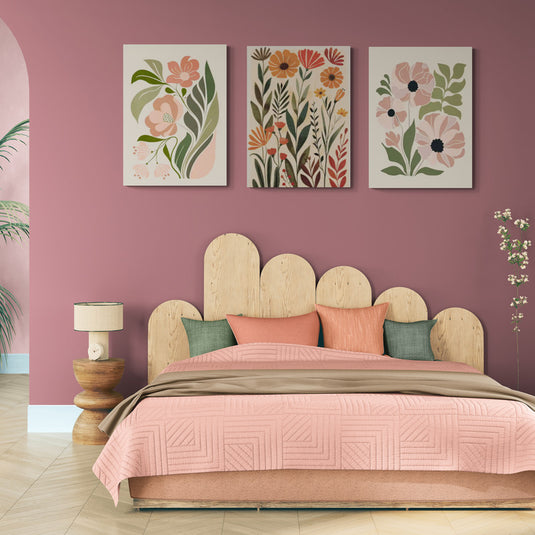 Set de tres cuadros decorativos con ilustraciones florales en tonos pastel sobre pared rosa en dormitorio moderno con cama de madera clara y ropa de cama rosa
