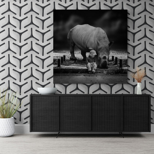 Cuadro decorativo blanco y negro de cuadro decorativo mostrando un rinoceronte y un niño sentado a su lado, ilustrando una escena de convivencia pacífica entre humanos y vida salvaje.