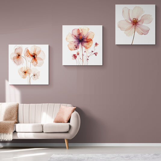 Trío de cuadros con flores acuareladas en tonos suaves sobre un fondo neutro, en un salón elegante con sofá blanco y detalles en rosa.