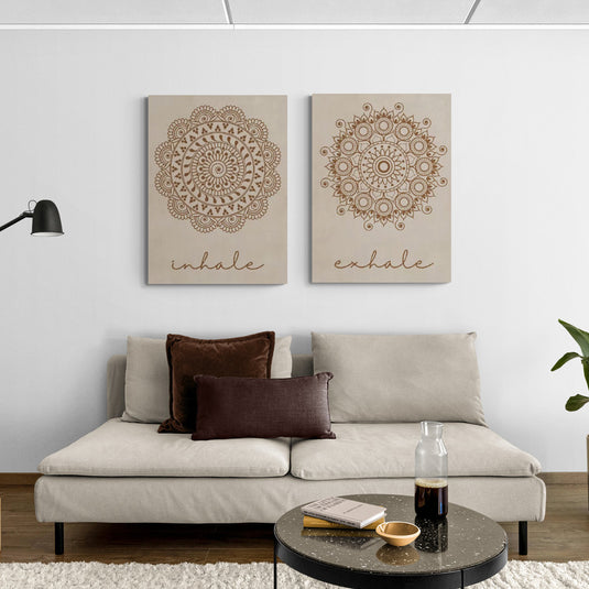 Dos cuadros de mandalas con las palabras 'inhale' y 'exhale' en un salón moderno, promoviendo calma y meditación con tonos beige y detalles dorados.