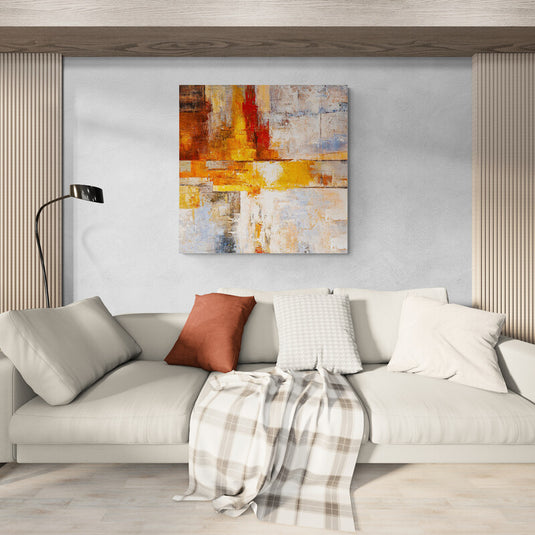 Arte abstracto en tonos cálidos de rojo, amarillo y blanco colgado en una sala moderna.