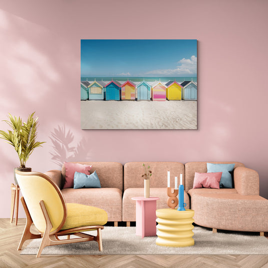 Lienzo decorativo de cabañas de playa coloridas sobre arena blanca bajo un cielo azul.