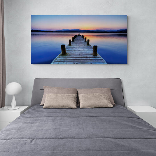 Fotografía de un muelle de madera al atardecer con montañas y un cielo colorido en el fondo