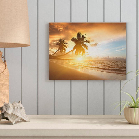 Fotografía de un amanecer en la playa con palmeras inclinadas y cielo anaranjado