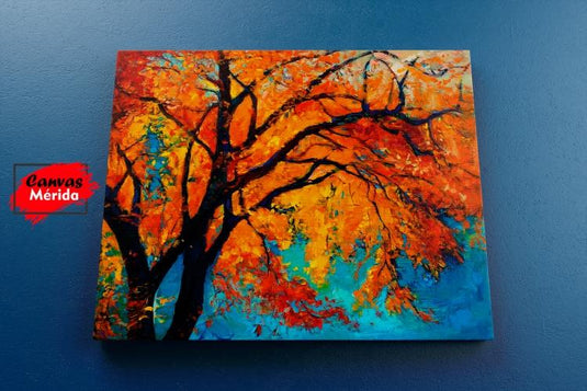 Cuadro decorativo con fondo azul, árbol delgado de tronco oscuro y hojas en tonalidades naranja y amarillo.