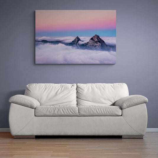 Paisaje montañoso envuelto en nubes bajo un cielo rosado y azul al amanecer.