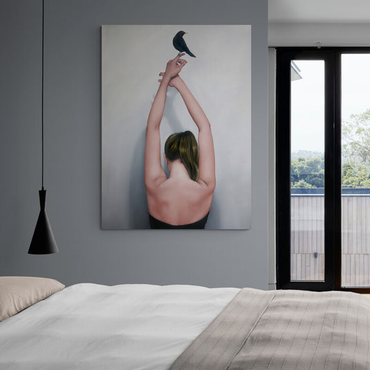 Mujer con blusa y espalda descubierta, cabello recogido café, manos alzadas con pájaro negro posado - cuadro decorativo en fondo gris