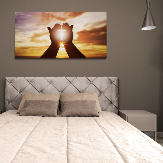 Manos en oración sosteniendo una cruz con luz al atardecer