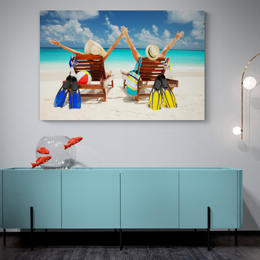 Dos personas con sombreros en tumbonas de playa celebrando, con aletas y pelota