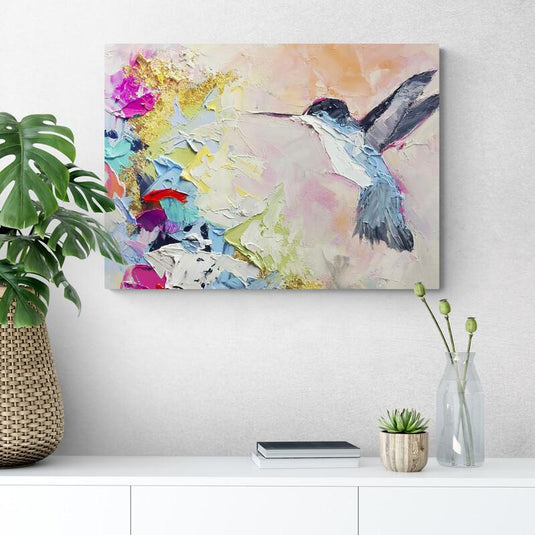 Cuadro con fondo pastel rosa y naranja, explosión cromática en fucsia, verde y azules a un lado y colibrí azul, gris y blanco al otro