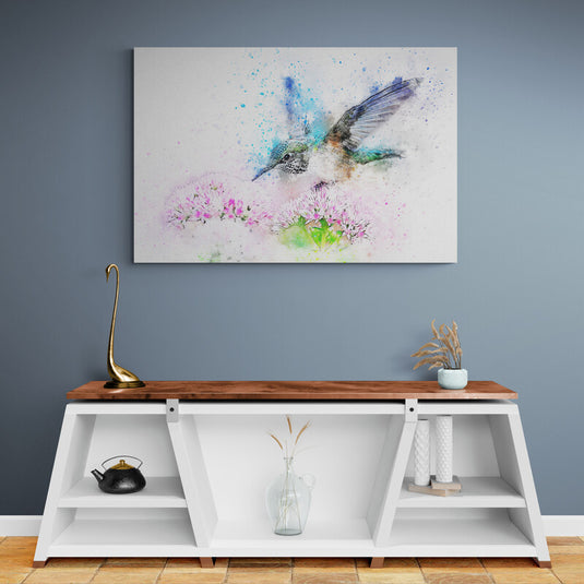 Colibrí acuarela en tonos azules, verde, morado, café y negro sobre fondo blanco, acompañado de flores rosadas y hojas verdes