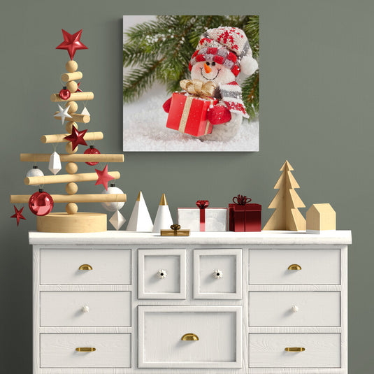 Muñeco de nieve con gorro sosteniendo regalo en ambiente nevado