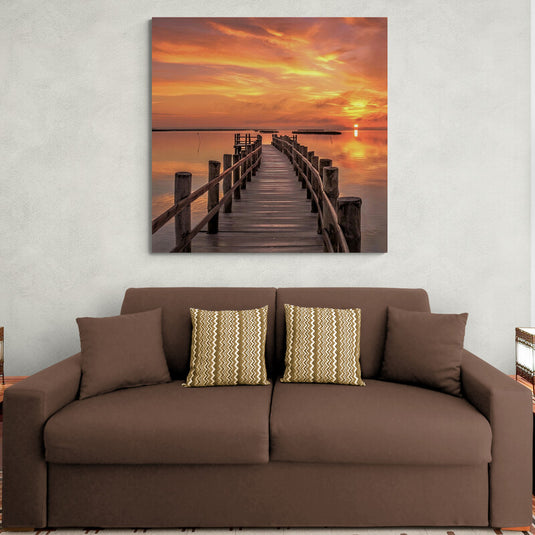 Fotografía de un muelle de madera al amanecer con cielo colorido y sol reflejado en el agua