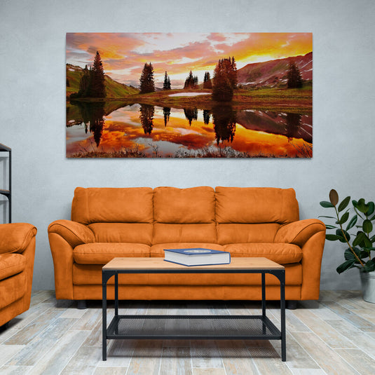 Fotografía artística de un campo con árboles y pinos, montañas al fondo, charcos reflectantes, bajo un vibrante atardecer de tonalidades cálidas