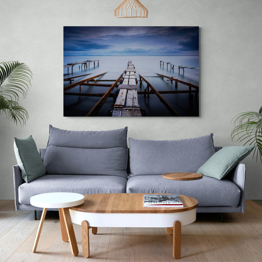 Fotografía de larga exposición de un muelle abandonado sobre aguas tranquilas bajo un cielo nublado.