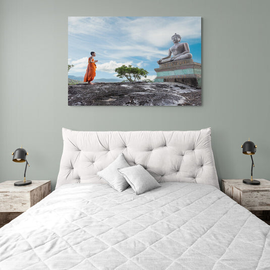 Monje budista orando frente a una gran estatua de Buda en un paisaje natural.