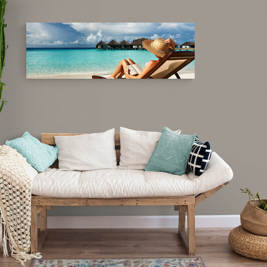 Persona relajándose en una tumbona de playa con sombrero, frente a bungalows sobre el agua