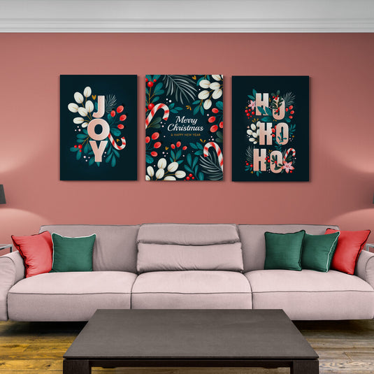 Set de cuadros navideños en fondo negro mate: 'JOY' con hojas verdes, blancas y rojas; 'Merry Christmas' con diseño festivo y bastón de azúcar; 'HO HO HO' con temática navideña.
