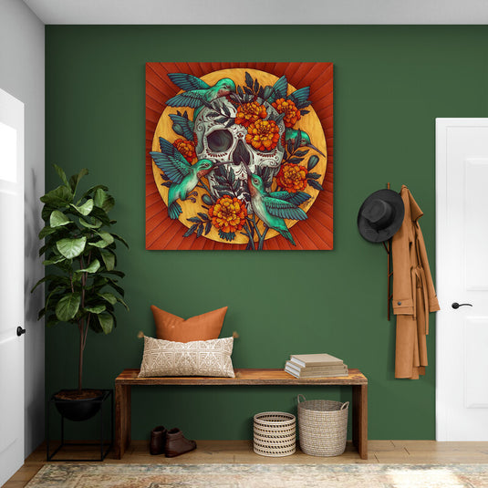 Cuadro con fondo naranja, círculo amarillo conteniendo calavera, rodeado de colibríes turquesa y flores de cempasúchil