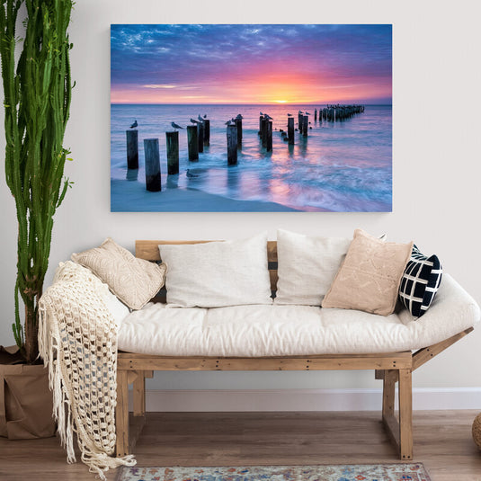 Fotografía de muelle con aves al amanecer y cielo colorido reflejado en el agua