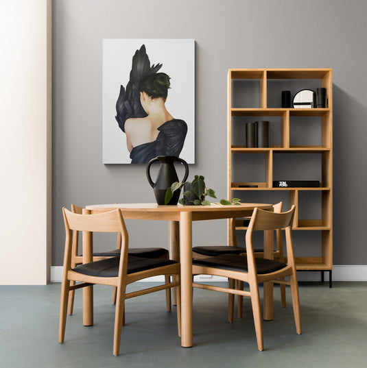 Mujer de espaldas con alas negras y cabello recogido frente a ala detallada en cuadro decorativo blanco