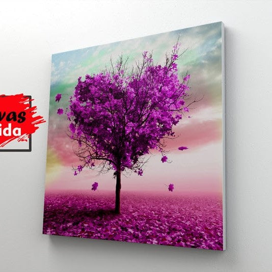 Cuadro decorativo de un árbol de tronco oscuro con hojas formando un corazón fucsia, hojas esparcidas en el suelo, bajo un cielo azul, verde, rosa y con toques de amarillo