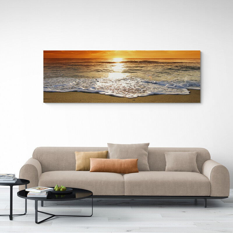 Fotografía de un amanecer con el sol reflejado en las olas y la arena dorada