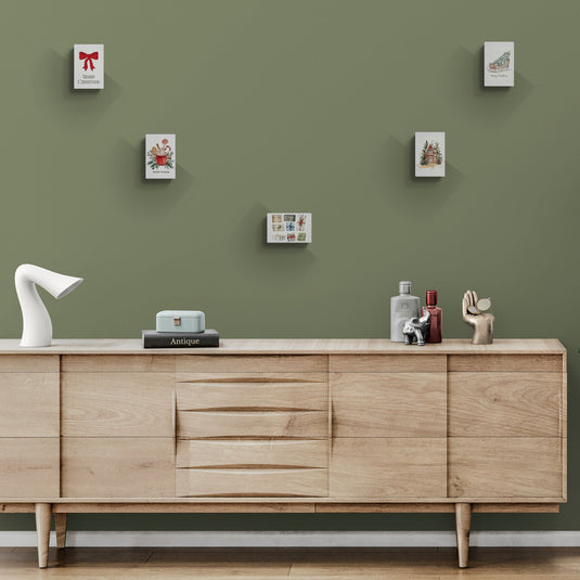 Lienzos navideños con motivos festivos y decoración escandinava sobre mueble de madera clara.