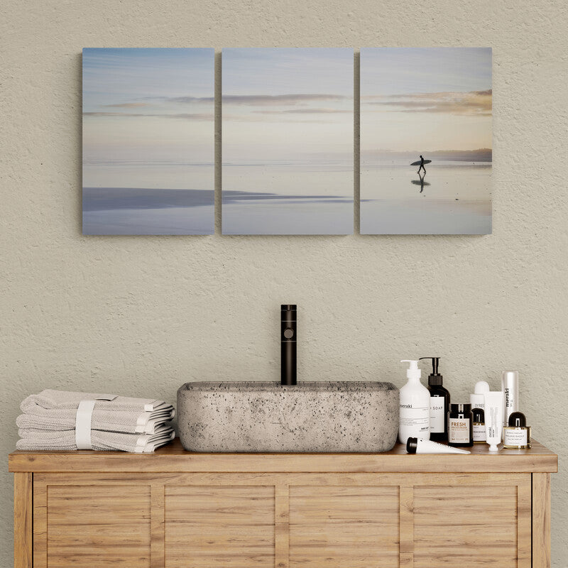 Fotografía tranquila de un surfista al amanecer con pilares reflejados en la playa tranquila