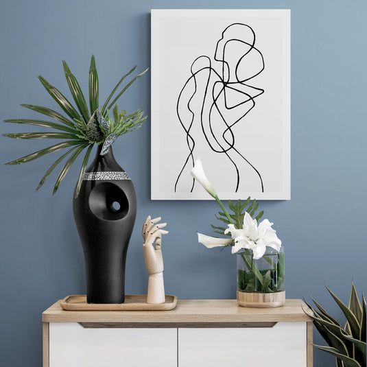 Cuadro minimalista con siluetas abstractas en blanco y negro decorando una pared azul pastel con plantas y objetos decorativos.