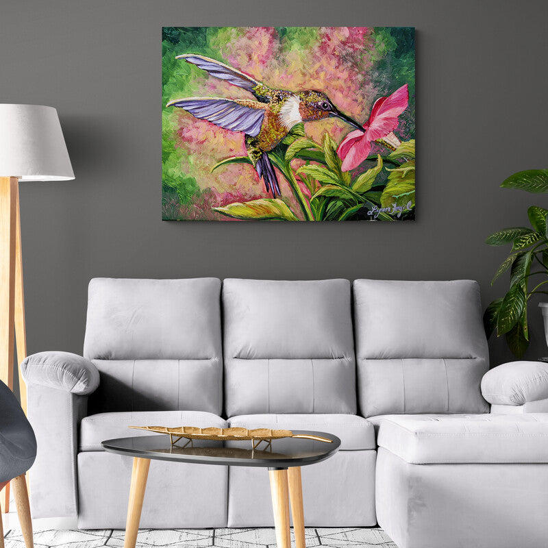 Cuadro decorativo tropical: fondo en tonos verdes, rosas y arena, con hojas verdes, flor rosa y colibrí verde-café con alas moradas en plena alimentación