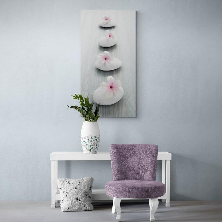 Cuadro decorativo con fondo gris, piedras circulares en fila y flores de mayo blancas con centro rosa sobre ellas.